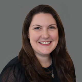 Smiling woman with long dark hair in a black blouse against a gray background
